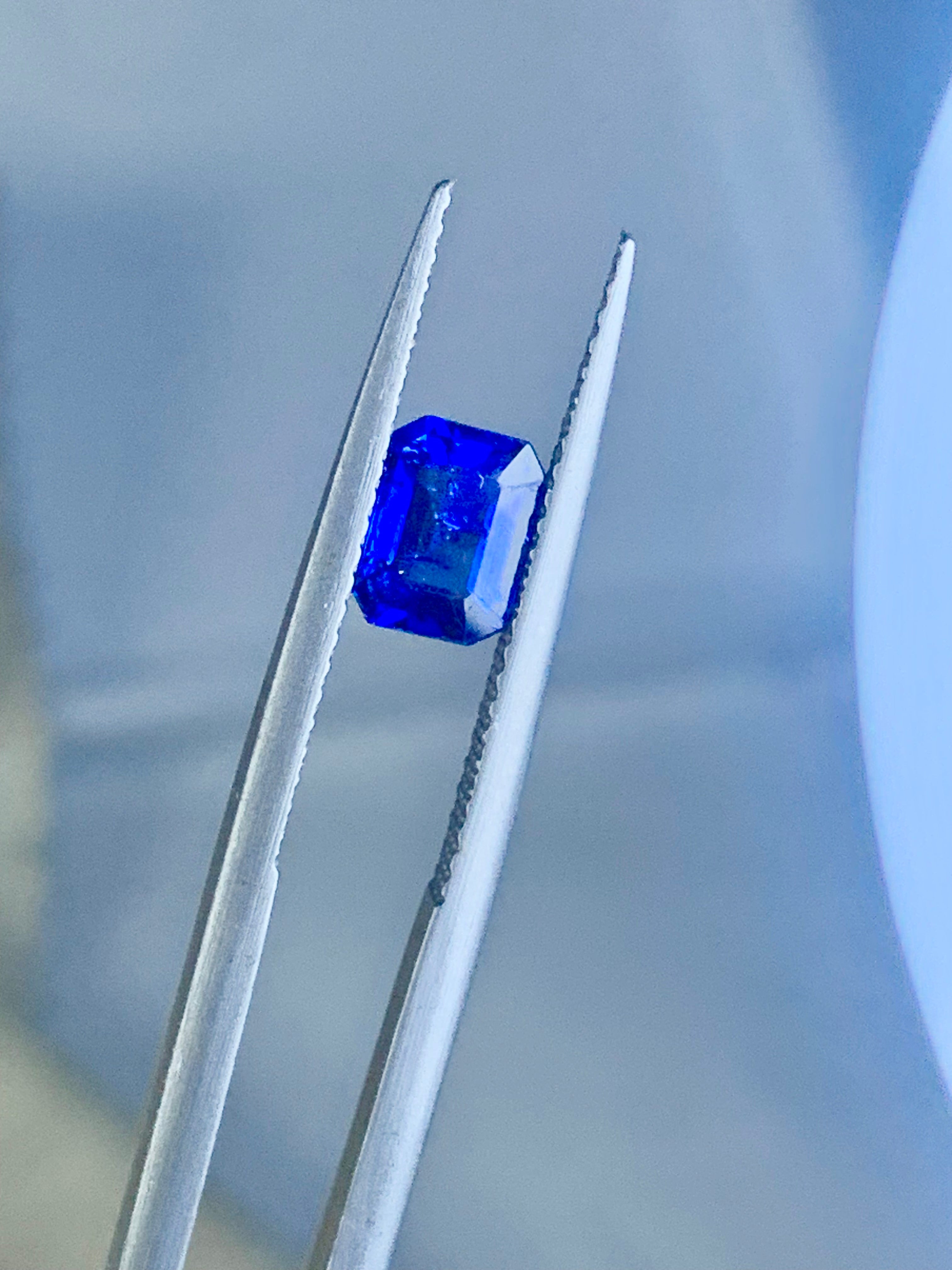 Blue gemstone held by tweezers against a blurred background