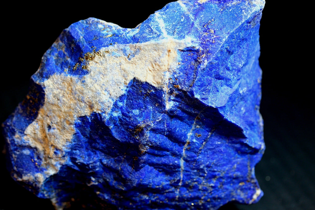 A raw blue lapis lazuli crystal specimen with prominent golden pyrite inclusions and beige matrix